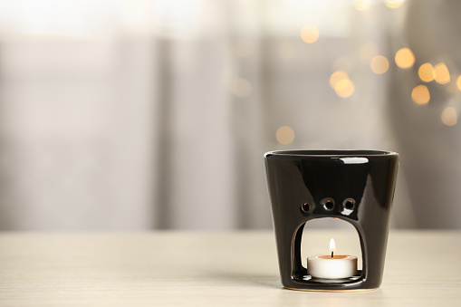 Aroma lamp with burning candle on table against blurred lights, space for text