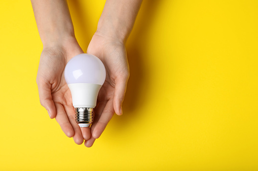 Woman holding light bulb on yellow background, top view. Space for text