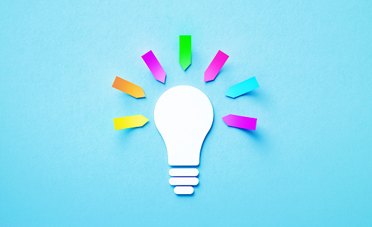 White lightbulb shape surrounded by colorful adhesive notes sitting over blue background. Horizontal composition with copy space.