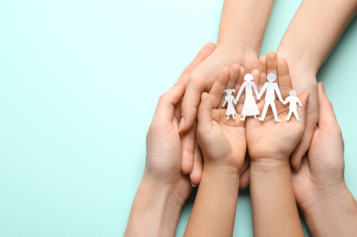 Parents and child holding paper cutout of family on light blue background, top view. Space for text