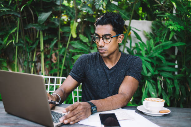 istock Pensive Hispanic freelancer browsing laptop at tropical cafe terrace 1408037721