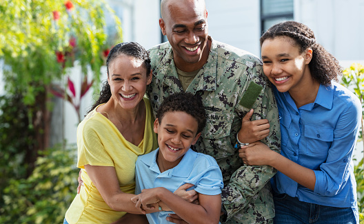 Portrait of a proud African-American navy veteran with his multiracial family, standing together outside their home. The two children and their mother are African-American and Caucasian. The parents are in their 40s, their daughter is 12 years old and their son is 8. Mother and daughter are smiling at the camera.