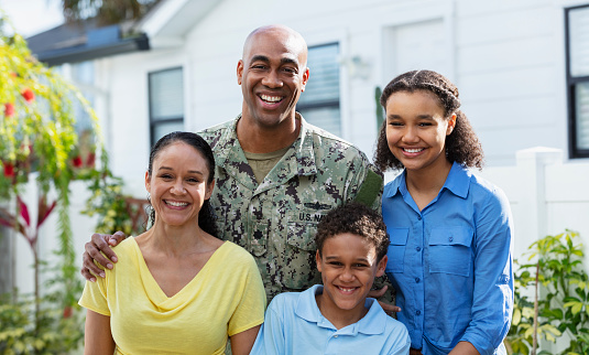 Portrait of a proud African-American navy veteran with his multiracial family, standing together outside their home. The two children and their mother are African-American and Caucasian. The parents are in their 40s, their daughter is 12 years old and their son is 8. They are all smiling at the camera.