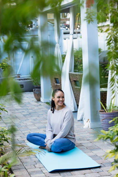 Woman sitting on exercise mat on patio, smiling stock photo