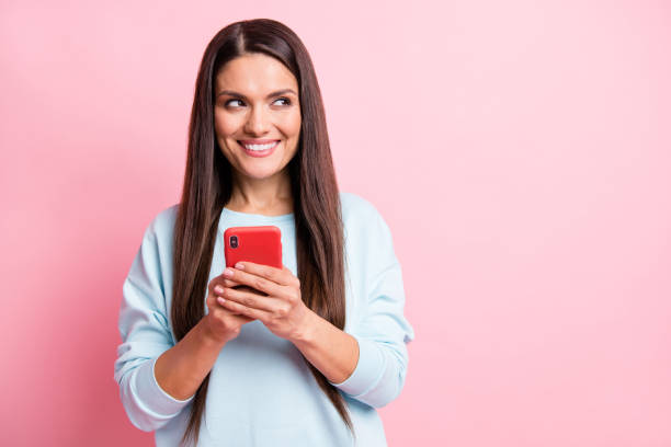 istock Photo portrait of brunette using cellphone texting sms looking empty space isolated on pastel pink color background 1408039016