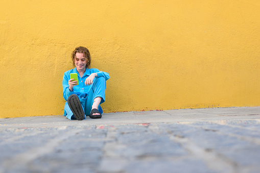 Young man in blue clothes with a mobile phone on a yellow wall
