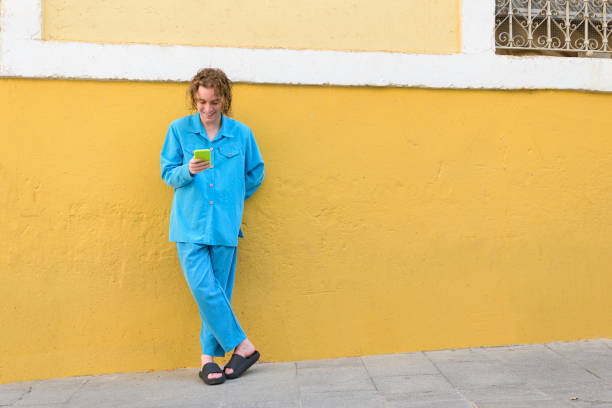 istock Young man in blue clothes with a mobile phone on a yellow wall 1408041626