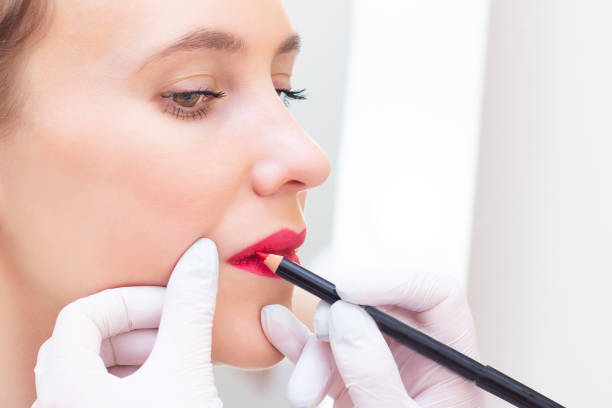 istock Young woman having permanent makeup on her lips at the beauticians salon. Permanent Makeup (Tattoo). drawing a contour with a white lip pencil 1408042157