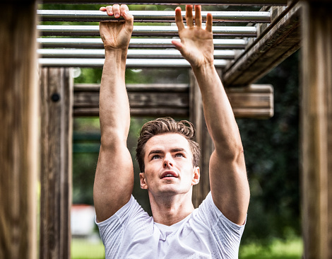 A man looking up as he progresses along the monkey bars on an outdoor obstacle course in a London park.