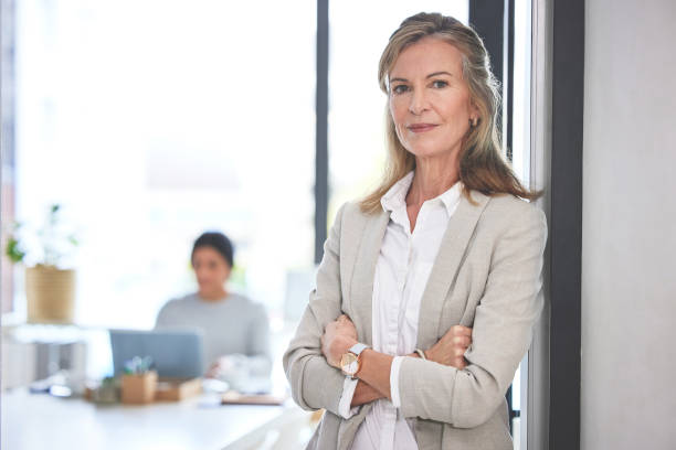 Proud entrepreneur standing with arms folded in the doorway entrance to boardroom. Confident corporate manager working at a startup company. Mature businesswoman standing with her arms crossed stock photo