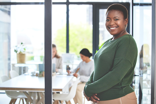 African business woman inside an office with copy space. Portrait of a happy female employee at the workplace with her team in the morning. Young lady smiling on her first day at work as an intern