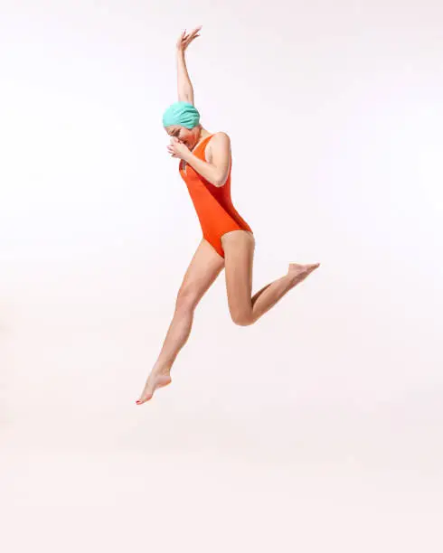 Photo of Portrait of young woman in swimming suit and cap jumping into water isolated over grey studio background