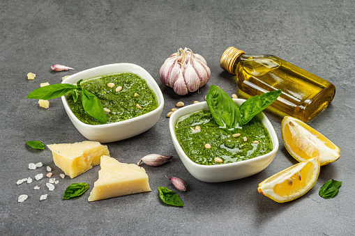 Pesto sauce in a bowls with pine nuts, parmesan and garlic. Traditional Italian food, grey stone concrete background, close up