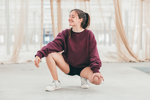 Young fashionable woman with property released handmade craft designer Sweater sitting & Laughing. Industrial hall with a curtain in the background. Millennial Generation Woman Young Fashion Design Portrait. Nontrivial