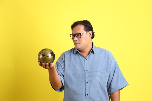 The adult Asian man with blue shirt standing on the yellow background.