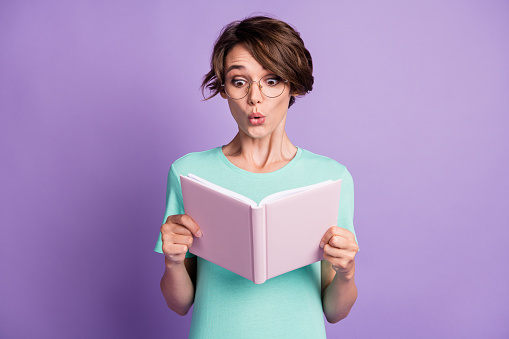Photo of cute impressed short brown hairdo lady read copybook wear spectacles blue t-shirt isolated on violet background.