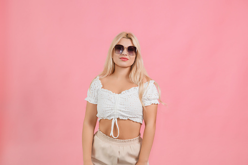 young fair girl in light clothes and glasses on a pink background