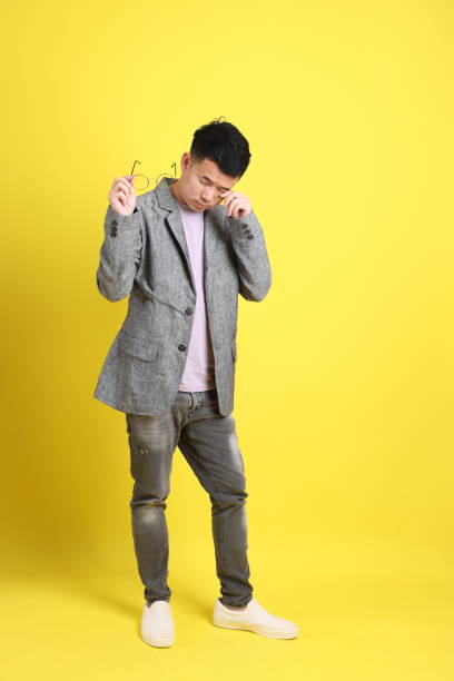 Man with Style The Asian LGBTQ man with grey blazer standing on the yellow background. human eye scratching allergy rubbing stock pictures, royalty-free photos & images