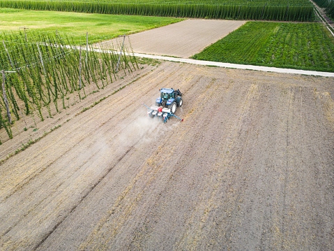 Aerial view of tractor sowing seeds in dry ground in field leaving behind cloud of dust. Drone shoots video planting and plowing grain agricultural machinery in soil.
