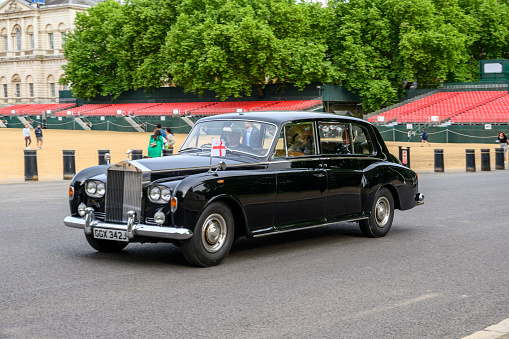 LONDON - May 18, 2022: Chauffeur driven Classic Rolls Royce with English flag passes Horse Guards Parade carrying well dressed passengers