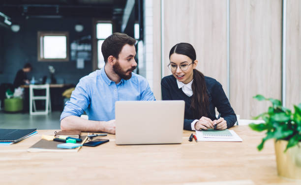 homme barbu regardant une femme surprise parcourant un ordinateur portable au bureau - computer business office occupation photos et images de collection