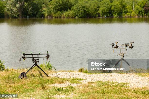 Rod Pods With Bite Indicators Holding Carp Fishing Rods Armed With Strong Reels On A Fishing Stand With Gravel On An European Lake Bordered By Trees During Summer Stock Photo - Download Image Now