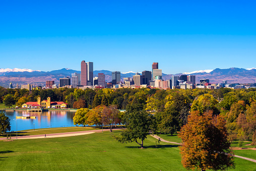 City skyline of Denver Colorado downtown with snowy Rocky Mountains and the City Park Lake.