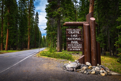 Welcome sign at the entrance to Crater Lake National Park in Oregon, located along the Volcanic Legacy Scenic Byway in a dense forest.