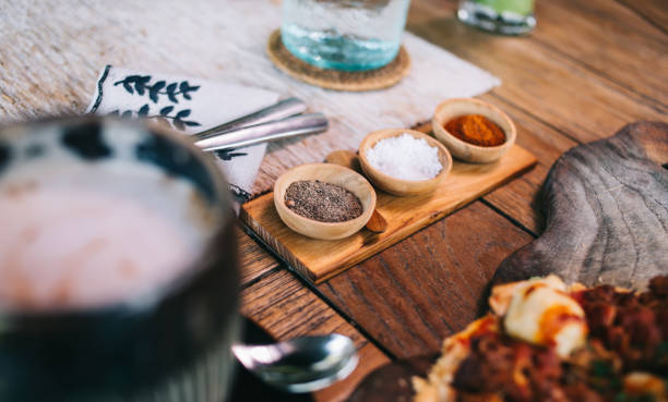 From above of bowls with salt black pepper and red pepper placed on wooden table in cafe near cup of coffee