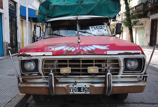 Buenos Aires, Argentina - January, 2020: Front view of old Ford F-100 pickup truck with red hood, rust on hood and bumper and argentinian license plate. Classic vintage pickup truck on street