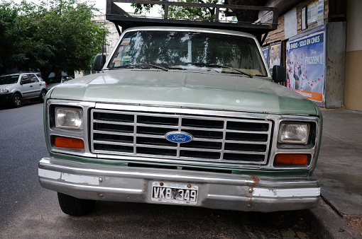 Buenos Aires, Argentina - January, 2020: Front view of radiator grille, headlights, hood and chrome bumper with rust of old classic american 80s Ford F-100 pickup truck with argentinian license plate