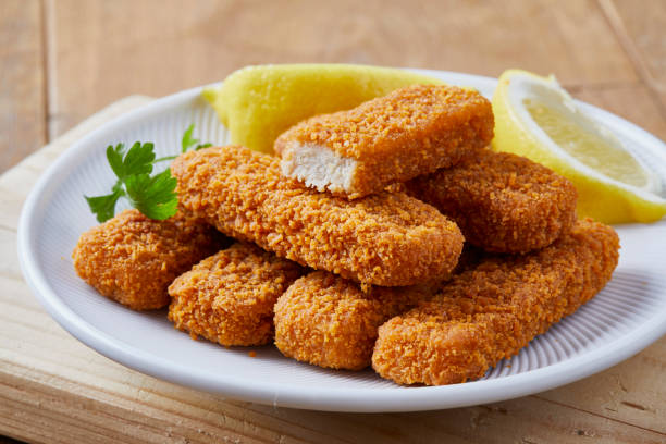 Fish sticks on a plate Close up of a fish sticks with lemon slices, served on a dark brown wooden kitchen table fish stick stock pictures, royalty-free photos & images