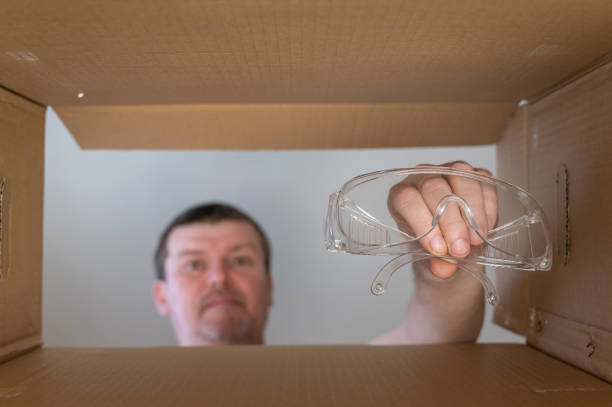 istock Man pulls safety glasses out of cardboard box for moving. Personal protective equipment. Bottom view. Inside view. Close-up. Selective focus. 1408057941