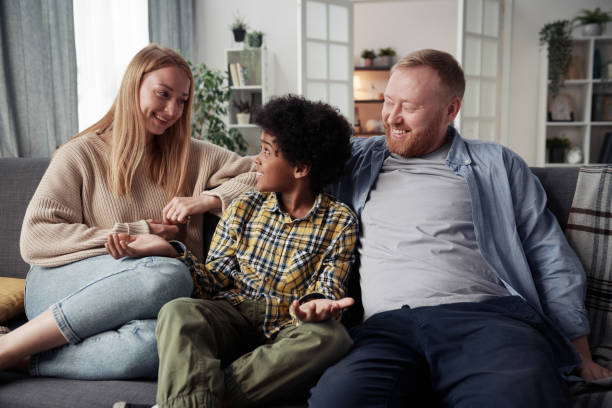 Parents spending time with their adoptive son Happy parents talking to their adoptive son African ethnicity while resting on sofa in living room foster care stock pictures, royalty-free photos & images