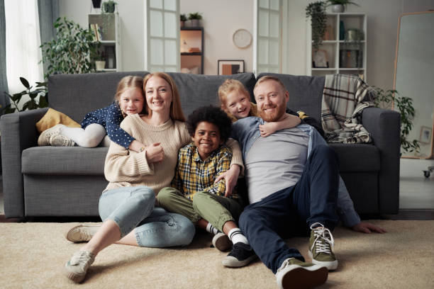 Happy family with adoptive children Portrait of happy parents with their adoptive children smiling at camera while resting together in living room at home adoption stock pictures, royalty-free photos & images