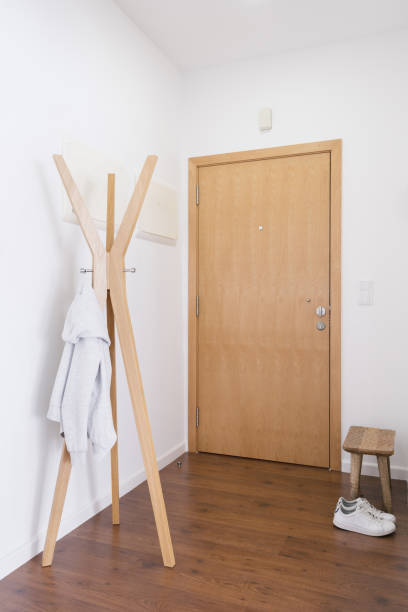 Light entrance hall area in modern apartment Entrance hall area in modern apartment. Vertical view of hallway with clothes on coat hanger, small handcrafted wood bench for shoes and wooden door in entryway coat rack stock pictures, royalty-free photos & images