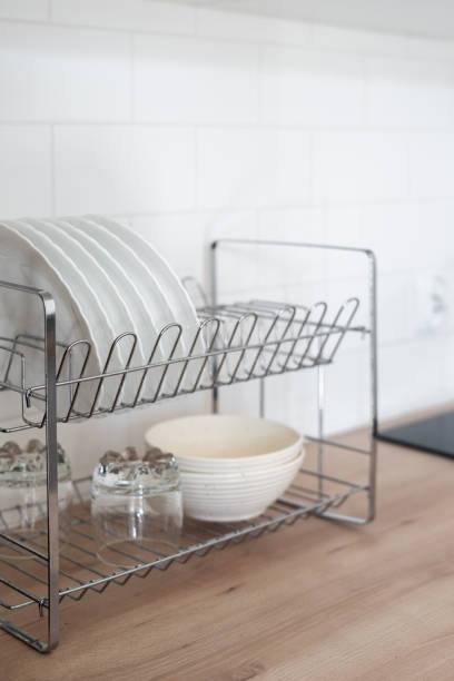 Side view of white clean plates and glasses in drainer after washing on tabletop. Home comfort. Cleanliness concept. Organizational space in kitchen