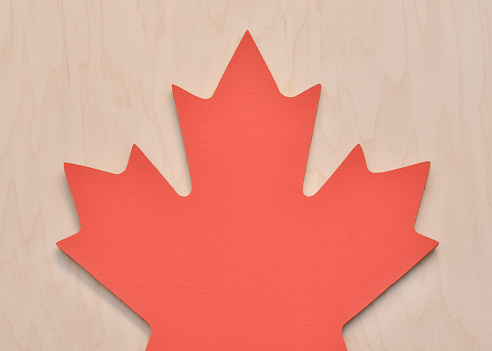 Closeup of a cork board in the shape of a red maple leaf on a wood background.