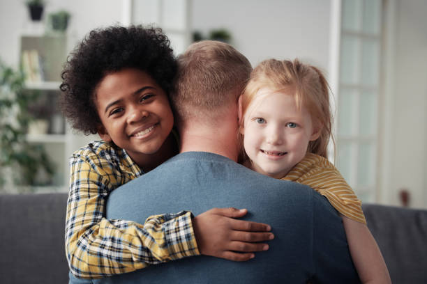 Happy adoptive children embracing father Portrait of happy multiethnic children smiling at camera while embracing their foster dad foster care stock pictures, royalty-free photos & images