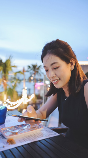 Luxury food lifestyle Asian generation Z women lifestyle enjoy fine dinning at chaopraya riverside using mobilephone photographing live social media with sunset scenics view restaurant in bangkok thailand
