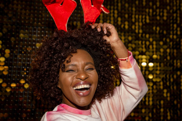 Christmas party-themed portraits on gold shiny sequence background shot in a studio. Happy mid-adult woman with a big afro hairstyle and a big smile. She is wearing Novelty reindeer antlers.