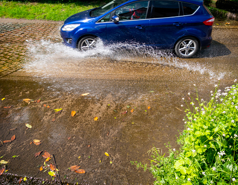 A blue car splashing through the ford which crosses the main street in Kersey, a small, pretty village in Suffolk, Eastern England, which is popular with tourists. The river is a tributary of the River Brett and the ford is locally known as “The Splash”.