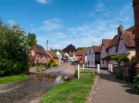 “The Street” in the pretty village of Kersey in Suffolk, Eastern England. The village, which gave its name to a type of cloth, has a long, winding and picturesque street of beautiful timber-framed medieval houses and a ford across a stream known locally as “The Splash”; it is highly popular with tourists as well as film companies.