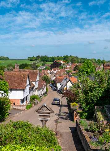 A view over the pretty village of Kersey in Suffolk, Eastern England, from the churchyard of St Mary’s parish church. The village, which gave its name to a type of cloth, has a long, winding and picturesque street of beautiful timber-framed medieval houses and a ford across a stream known locally as “The Splash”; it is highly popular with tourists as well as film companies.