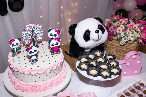 Children's birthday table with panda bear cake, sweets, and decoration with panda bear, pink heart and bouquet of flowers
