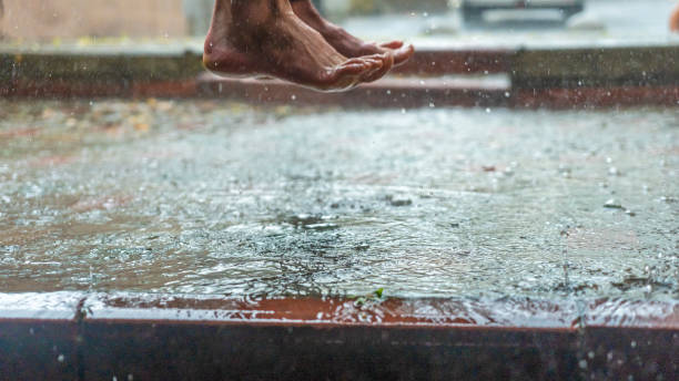 雨の中、水たまりを飛び越える人間の裸足。.選択的な焦点。テキスト用のスペース。雨滴が飛び散る。抽象的でファッション的な背景 - rain drenched one person standing ストックフォトと画像