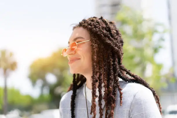 Women hipster with dreadlocks and pink sunglasses portrait outdoor side view. Close up headshot modern trendy female in city summer park