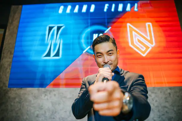 Asian Chinese Emcee Esports game show Host introducing grand final video game competition on stage with background projector screen
