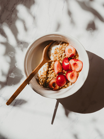 Healthy breakfast with greek yogurt, granola and cherry on bright background in sunlight and the shadows of the leaves of the tree, Health care, fitness, diet concept.