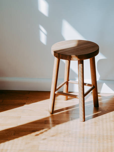 Brown wooden stool in room on parquet floor with shadows stock photo